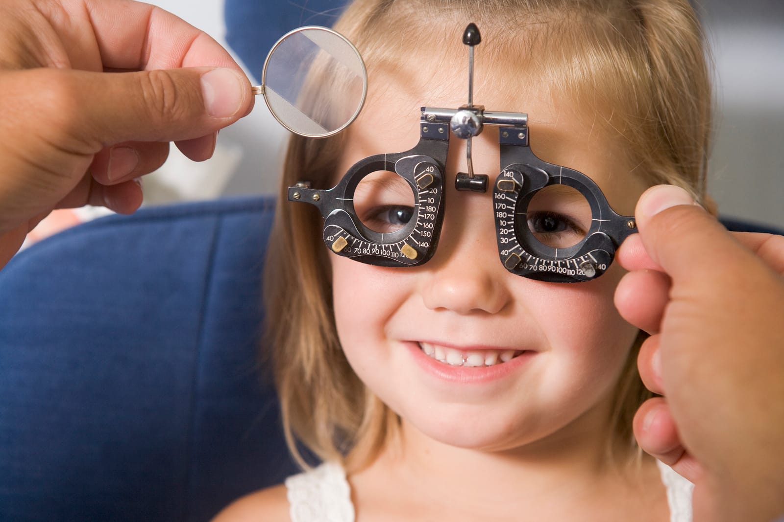 Optometrist giving an eye exam to a young girl sitting in a chair, smiling